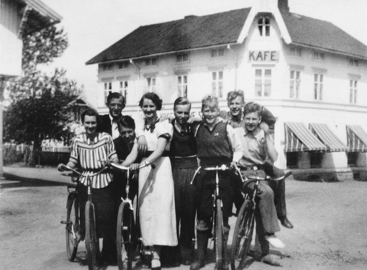 Anno Domkirkeodden, LØTEN SENTRUM, GRUPPE 8 MED SYKLER FORAN SAMVIRKELAGET. KAFE. ---- kommentar start ---- nr. 4 fra v. Mina Tangnes, f. Engemoen, gift med stasjonsmester Einar Tangnes. nr. 5 Harald Nordskogen nr 7 Kåre Madsen, gift med Astrid Sveen på Karud ---- kommentar slutt ----
