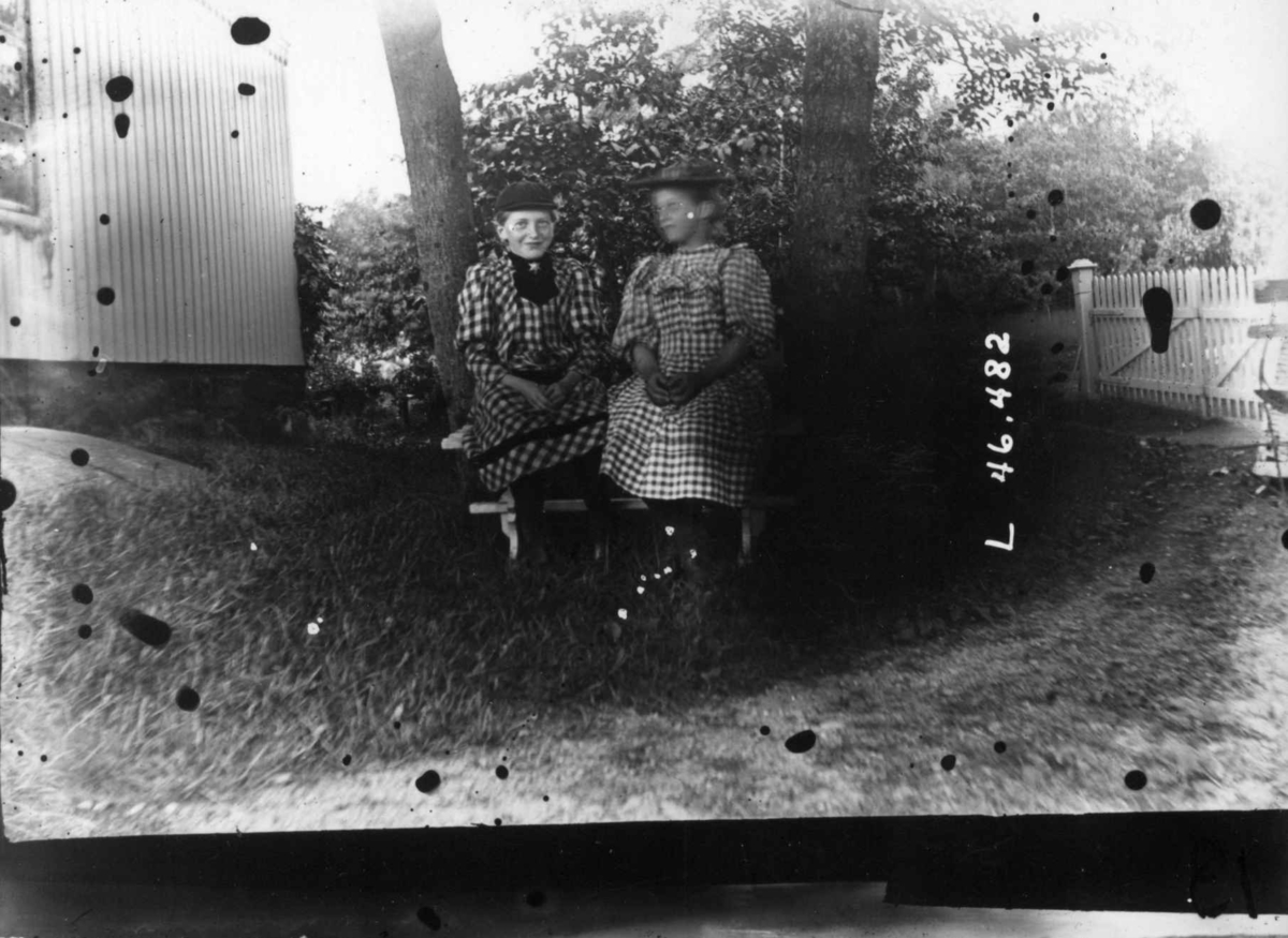 Hermann Christian Neupert, Drakt.1908-1910.To kvinner sittende i en hage. I kjoler og med hatter.