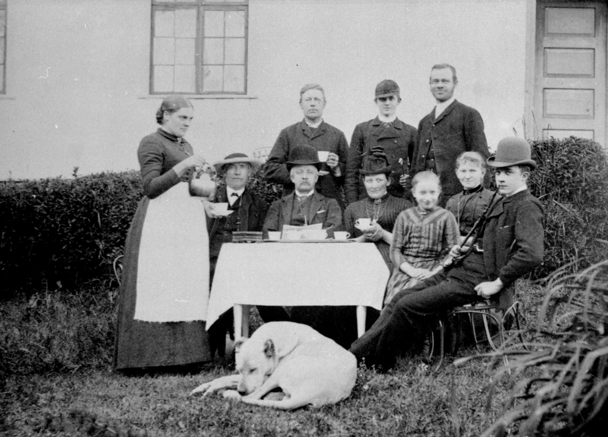 Anno Domkirkeodden, Familien Bjerke på Nerkvern, Brumunddal. Elen Olsen skjenker kaffe. Sittende er ukjent, Lars Bjerke, Ottilia Augusta Bjerke født Grüner, Lisbeth Bjerke med stripete kjole, Mina Maurud født Korning, Borger Bjerke med langpipe. Stående bak nummer 2 er Thore Christian Bjerke, Maurud.
