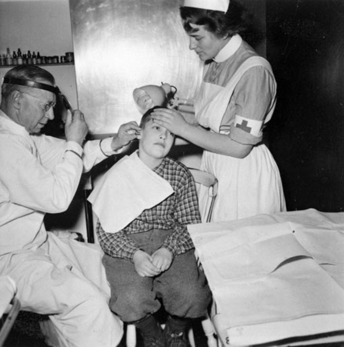 Anno Domkirkeodden, HAMAR RØDE KORS KLINIKK. LEGE ARVE MELLUM UNDERSØKER ØRET TIL GUTT. SØSTER HELGA ASSISTERER.