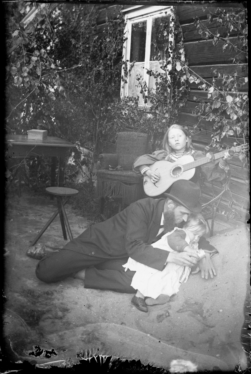 Skötsner-Edhlund, Ruth Skötsner spelar gitarr, Per Elis och Josef Edhlund leker i sandhögen, Östhammar, Uppland