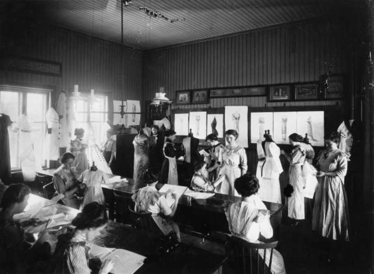Marthinius Skøien, Klasse i kjolesøm, antatt Oslo, antatt tidlig 1900-tall.. Kvinner i aktivitet i klasserom.