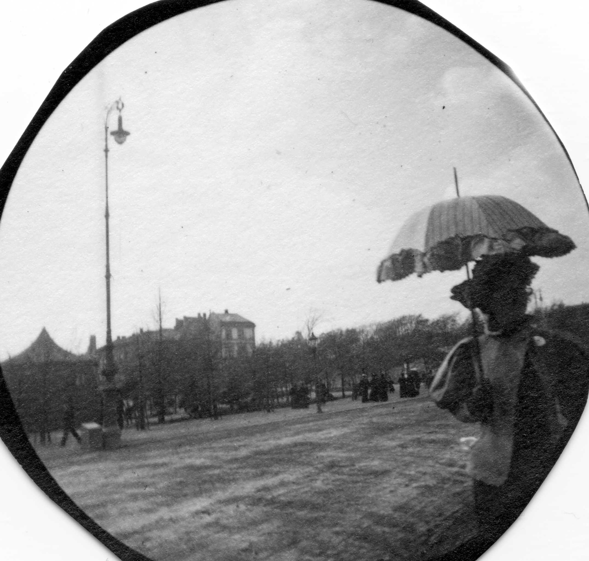 Fredrik Carl Mülertz Størmer, Kvinne med parasoll spaserer i park, Oslo. Bygårder i bakgrunnen.