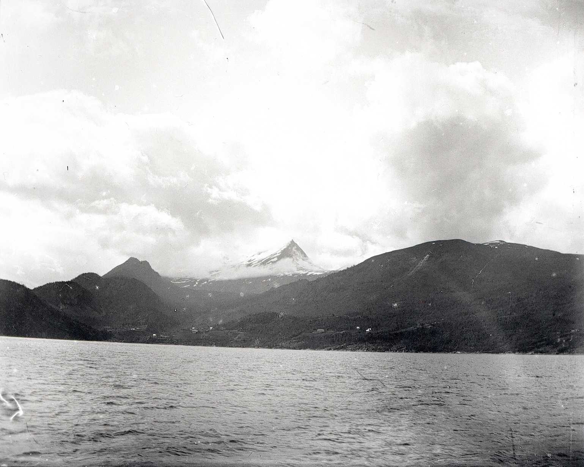 Tom Kent, Bilde tatt fra sjøen mot fjellandskap. Spiss snødekket tind med skyer.