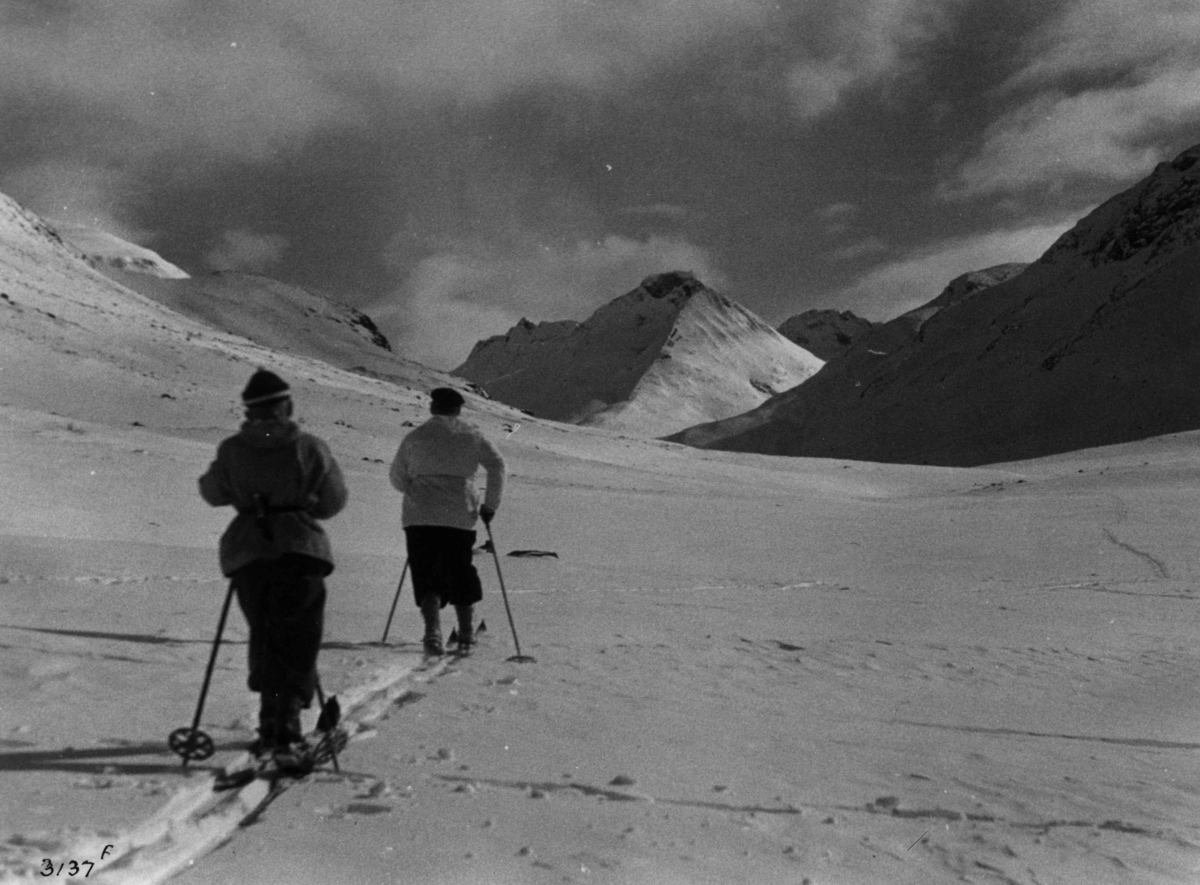Anders Beer Wilse, Skiløpere i Visdalen i Jotunheimen med snødekte fjell og sol.