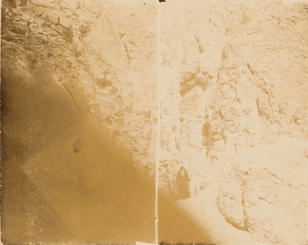 Unknown, [Man standing at base of cliff wall]