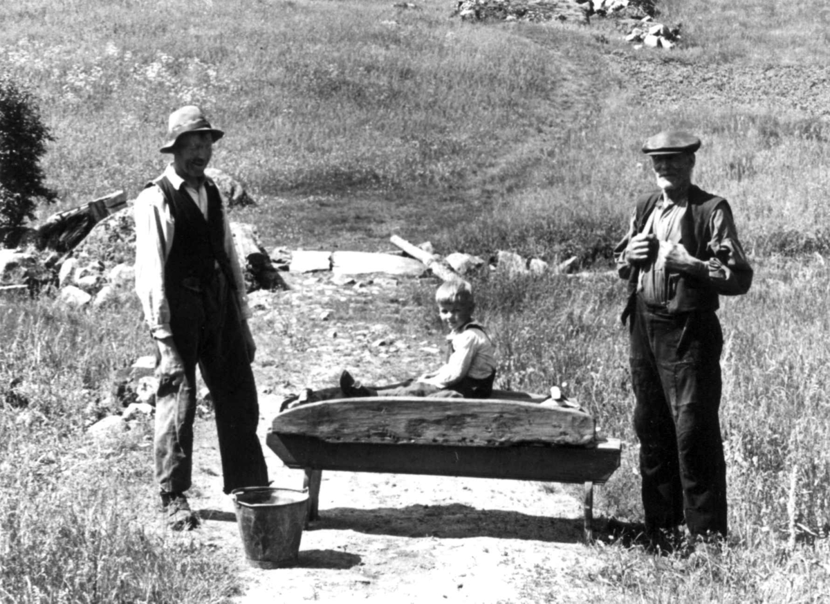 Anna Grostøl, To menn står ved en stampe, en gutt sitter oppå den. Fjotland, Kvinesdal, Vest-Agder 1941.