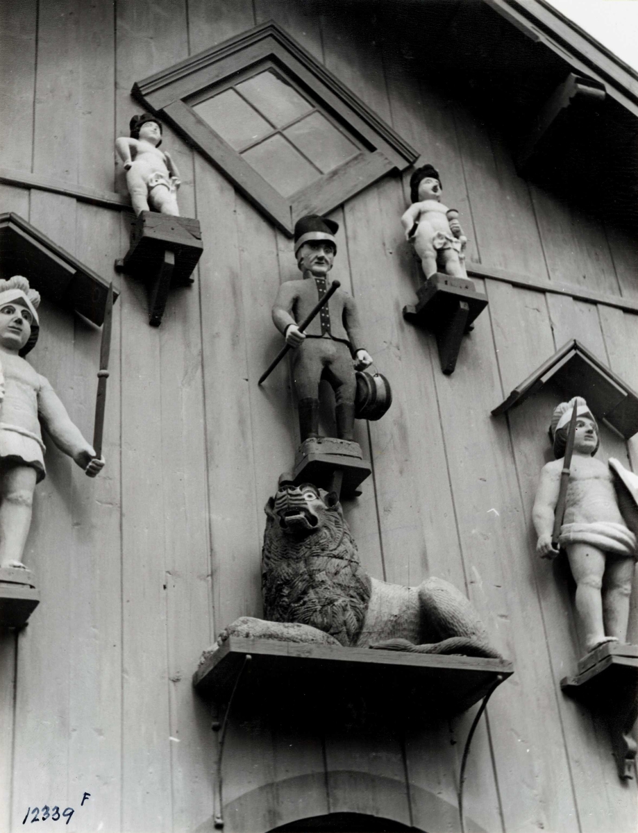 Anders Beer Wilse, Lensmannsgården Østgård, Tolga, Hedmark ant. ca. 1940. Detalj av stabbur med trefigurer på fronten, figurene skal være laget av fanger.