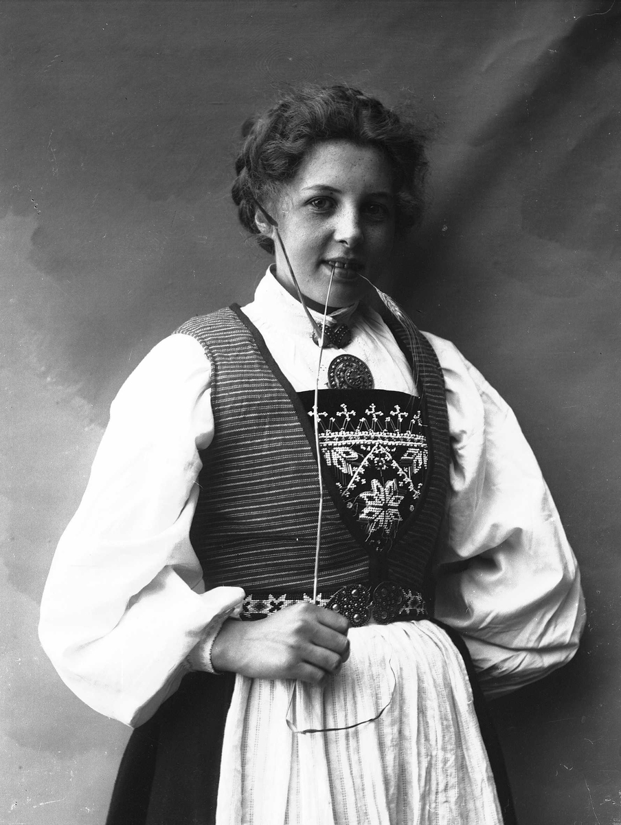Solveig Lund, 1/2 dels studioportrett av kvinne i drakt, med oppsatt hår. Hun biter på et strå hun holder i høyre hånd. Hun er avfotografert mot en nøytral bakgrunn.