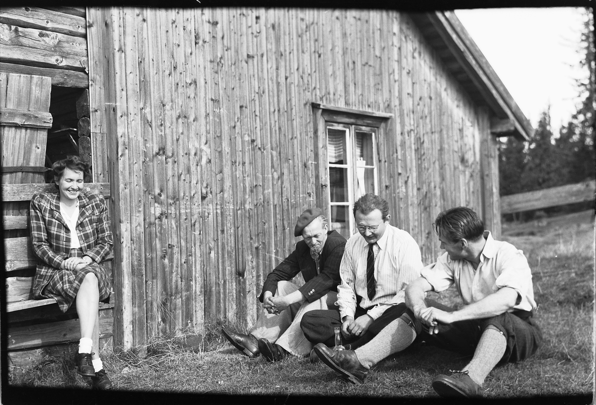 Håkon Prestkværn, Fra venstre, Ingeborg Haugen, sittende på en krakk, ukjent, Lars R. Haugen, som var bestyrer på Moelven Meieri 1945-65. Ukjent. Sitter på bakken å stirrer på en tom flaske foran en hyttevegg.