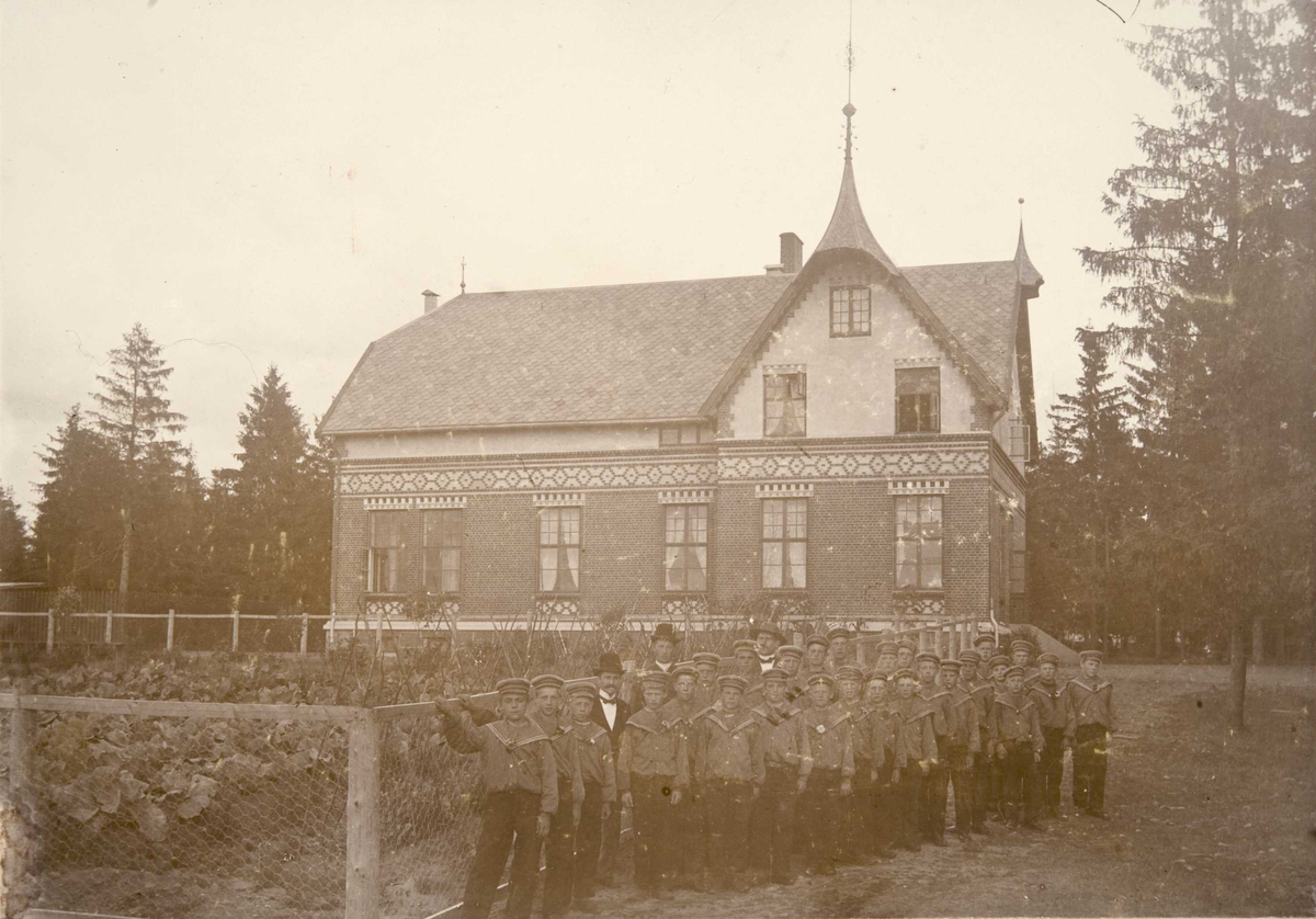 Berg & Høeg, Internatbygningen Breidablikk på Bastøy skolehjem, Bastøya, ca. 1903. Elever står oppstilt utenfor bygningen.