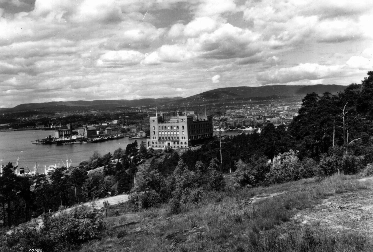 Hermann Christian Neupert, Sjømannsskolen, Ekeberg, Oslo 1936. Oversiktsbilde. Utsikt over Oslo fra Ekeberg med Sjømannsskolen midt i bildet. Skog og åser i bakgrunnen.