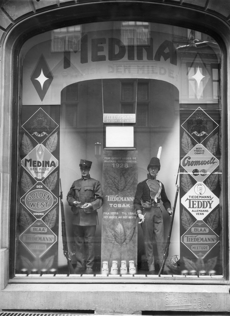 Narve Skarpmoen, Vindusutstilling med reklame for Tiedemann. To utstillingsdukker med militæruniformer røyker pipe og sigarett. Man viser også en film som er optatt under de militære festligheter 1928.
