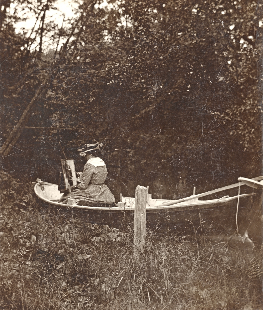 Unknown artist, Konstnärinnan Josefina Holmlund i färd med ett landskapsmotiv vid ett besök på prästgården Korsnäs omkring förra sekelskiftet. Bostället disponerades vid tiden av den konstnärligt intresserade och utövande kyrkoherden Gustaf Leonard Lundqvist och dennes maka Jacuette. Möjligtvis är det den fotointr…