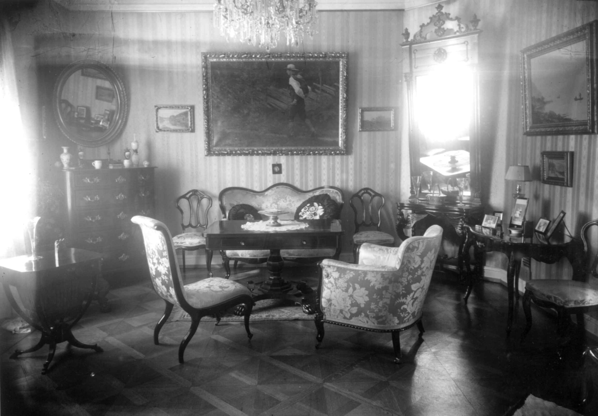 Hermann Christian Neupert, Trapp-Mayer. Stueinteriør 1925. Sofa med bord og stoler. Speil og malerier på veggene. Lysekorne.