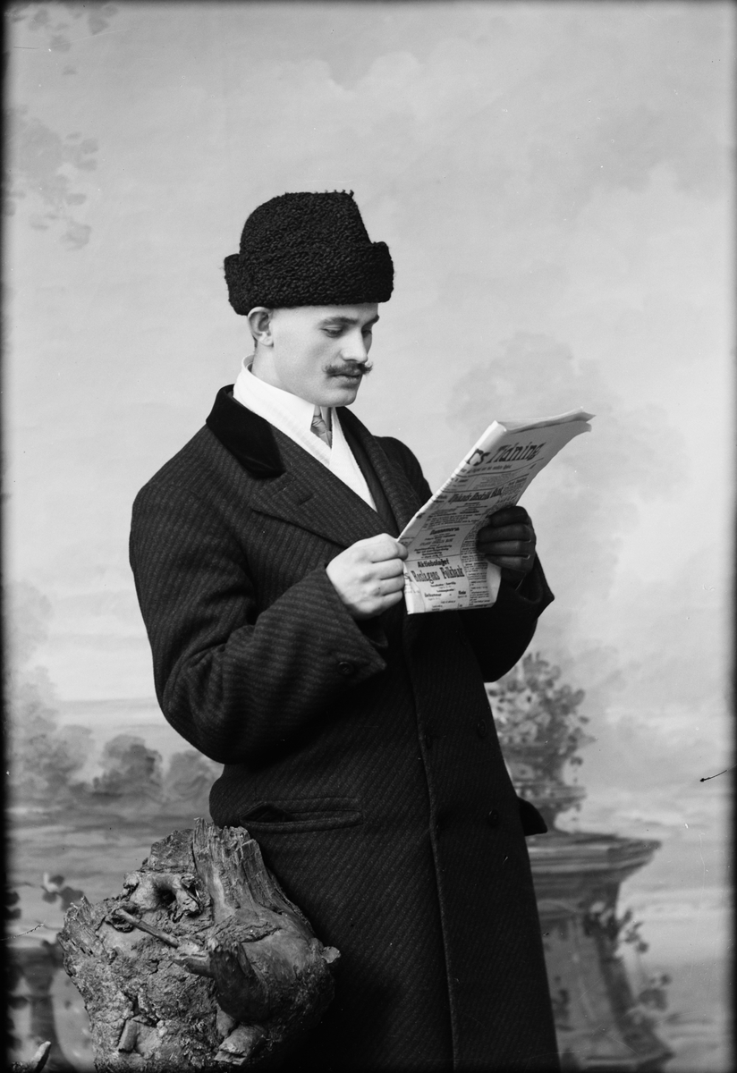 Skötsner-Edhlund, Ateljéporträtt - man i ytterkläder står och läser tidning, Östhammar, Uppland