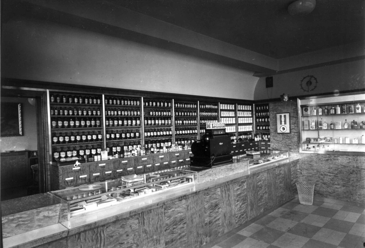 Hermann Christian Neupert, Rådhusapoteket, Oslo. 1937. Interiør. Utsalg. Disk. Hyller med apotekervarer på flasker og i krukker.