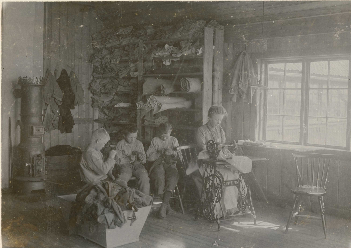 Berg & Høeg, Skredderverkstedet på Bastøy skolehjem, Bastøya, Horten kommune, ca. 1903. Tre elever og en kvinnelig ansatt sitter og syr.