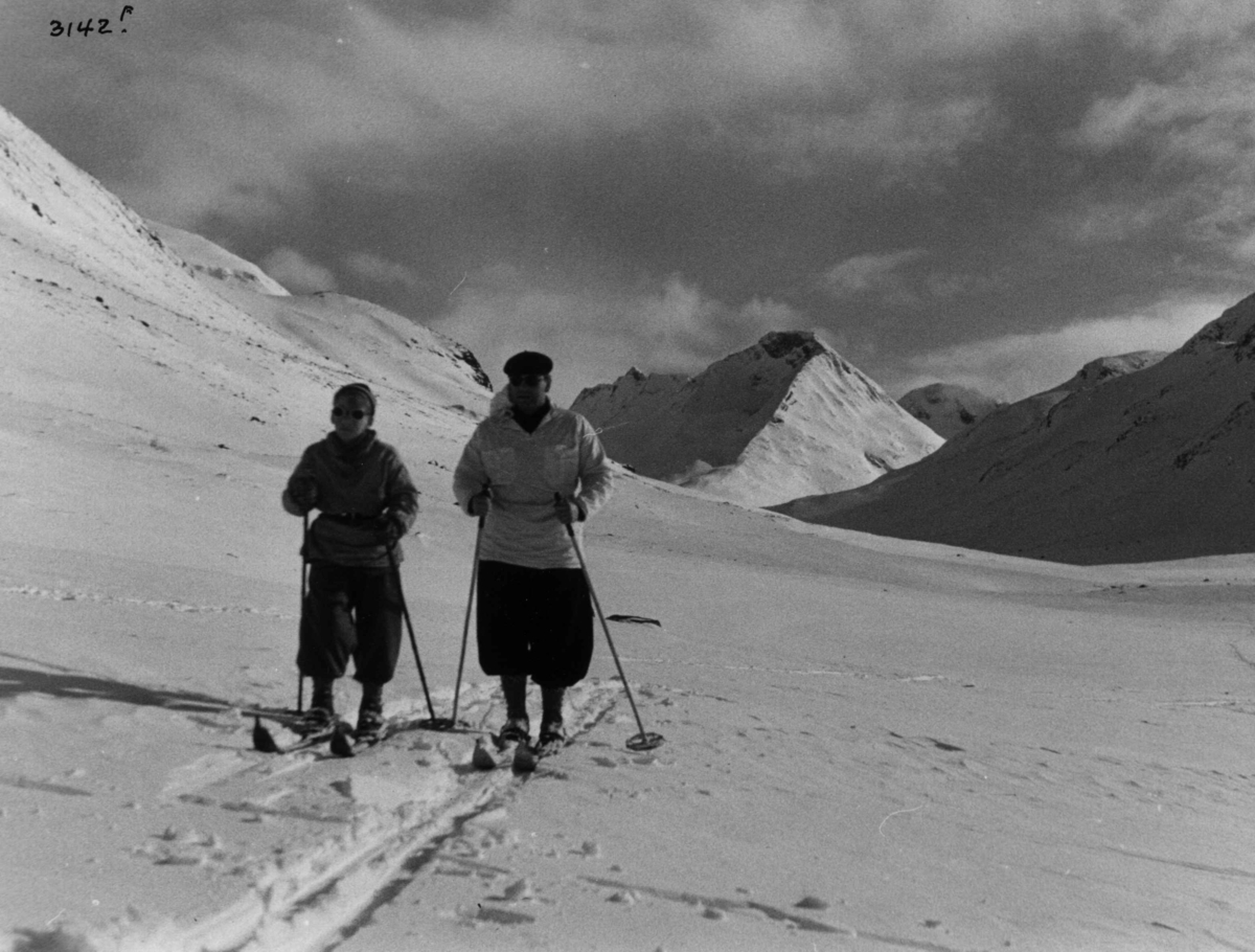 Anders Beer Wilse, Skiløpere i Uladalen i Jotunheimen med snødekte fjell og sol.