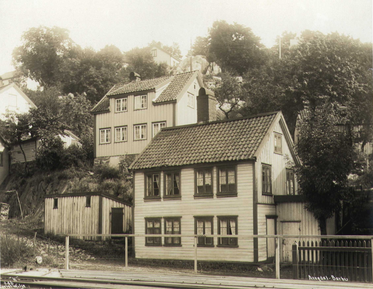 Anders Beer Wilse, Bolighus, Barbu, Arendal, Aust-Agder. Fotografert 1912. Husene i bildet eksisterer fremdeles og har adressene Barbu 18 (foran) og Barbu 22 (bak). I forgrunnen sees NSBs havnespor fra Arendal stasjon til godsstasjonen i Barbu, og jernbanekaia ved Barbubukt.