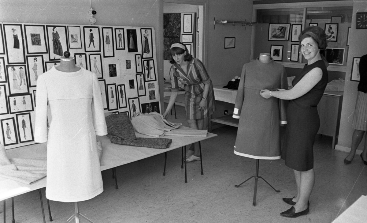Örebro Kuriren, Modeuppvisning, Krämaren, Gesällprov. 12 maj 1966 Två kvinnor klädda i korta klänningar samt med hårband i befinner sig i en syateljé. Kvinnan till vänster står och känner på tyger medan kvinnan till höger arbetar med en kort klänning som är upphängd på en provdocka. Till vänster syns en provdocka …