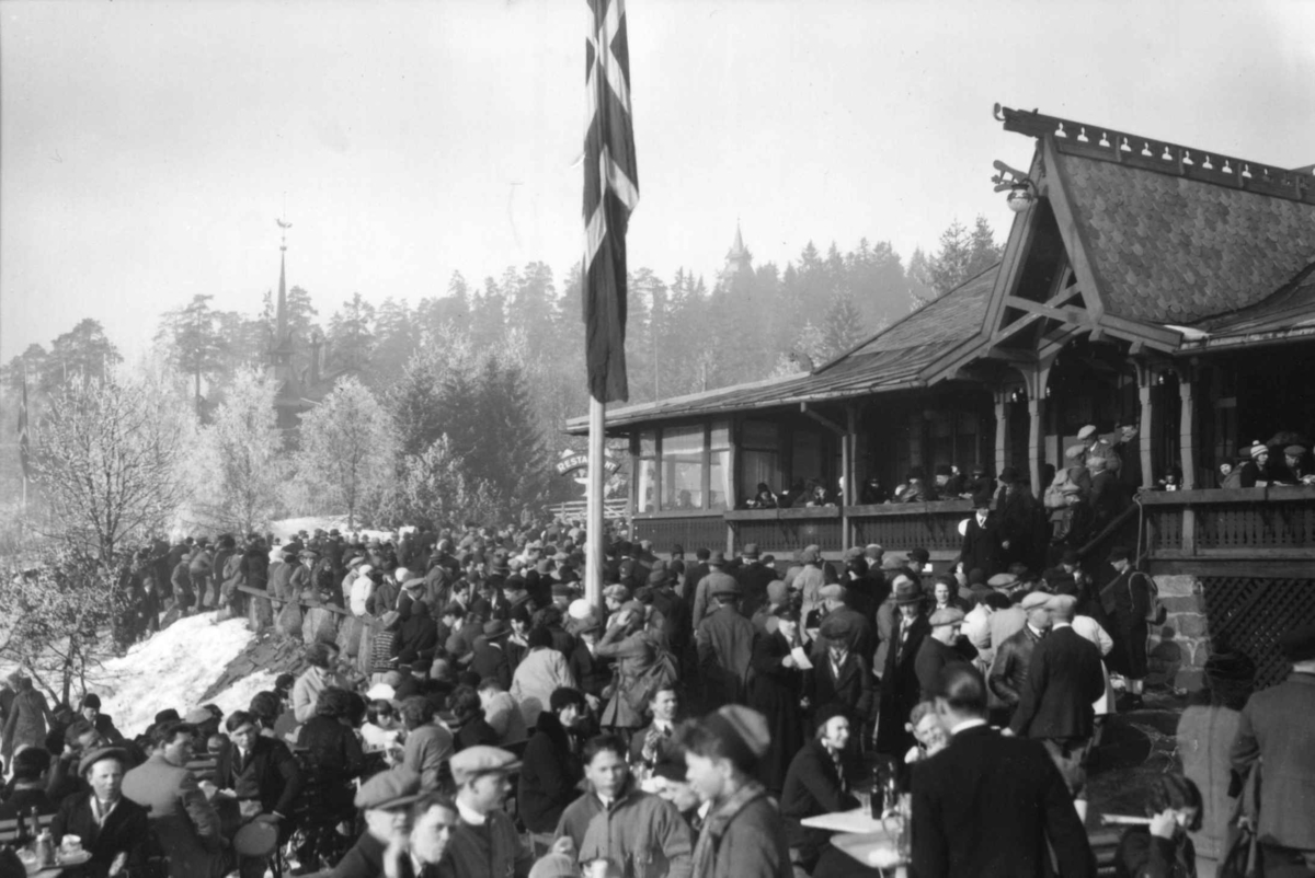 Hermann Christian Neupert, Frognerseteren - Oslo. Vintermotiv. Mennesker samlet foran restauranten. Flaggstang med flagg.