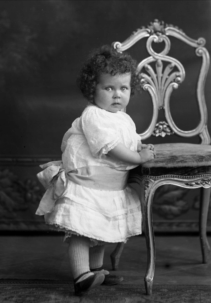 Gustav Borgen, Portrett av Laila Aavatsmark i kjole ved stol. Piken er oberstløytnant Aavatsmarks datter.