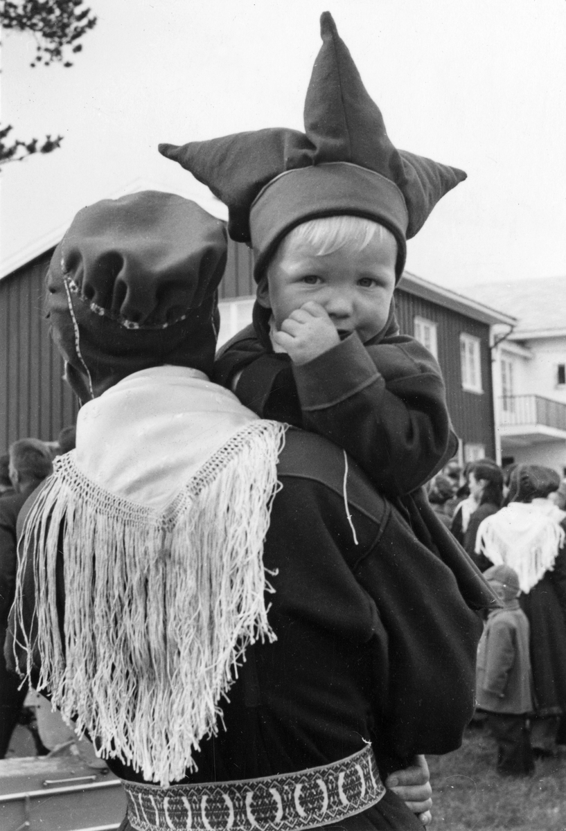 Virginia Raymond Davidson, Karasjokdrakt. Liten gutt titter over skulderen til "mor". Karasjok 1959. Fotografert den dag Kong Olav og prinsesse Astrid besøkte Karasjok.