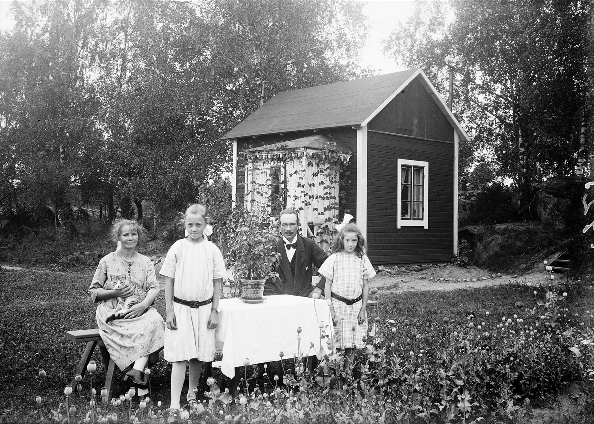 Bröderna Östlings foto AB, Familj framför sitt fritidshus, sannolikt Uppland 1925. Rabatt med vallmo som gått i frö i förgrunden