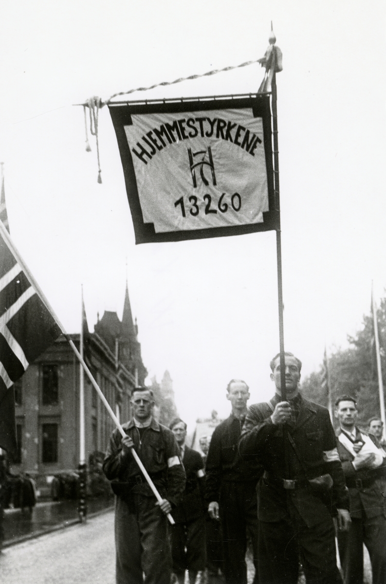 Anders Beer Wilse, Fra fredsdagene i 1945. Fra Borgertoget. Hjemmestyrkene marsjerer på Karl Johans gate. Fane med kongens monogram og teksten HJEMMESTYRKENE og nummeret 13260.