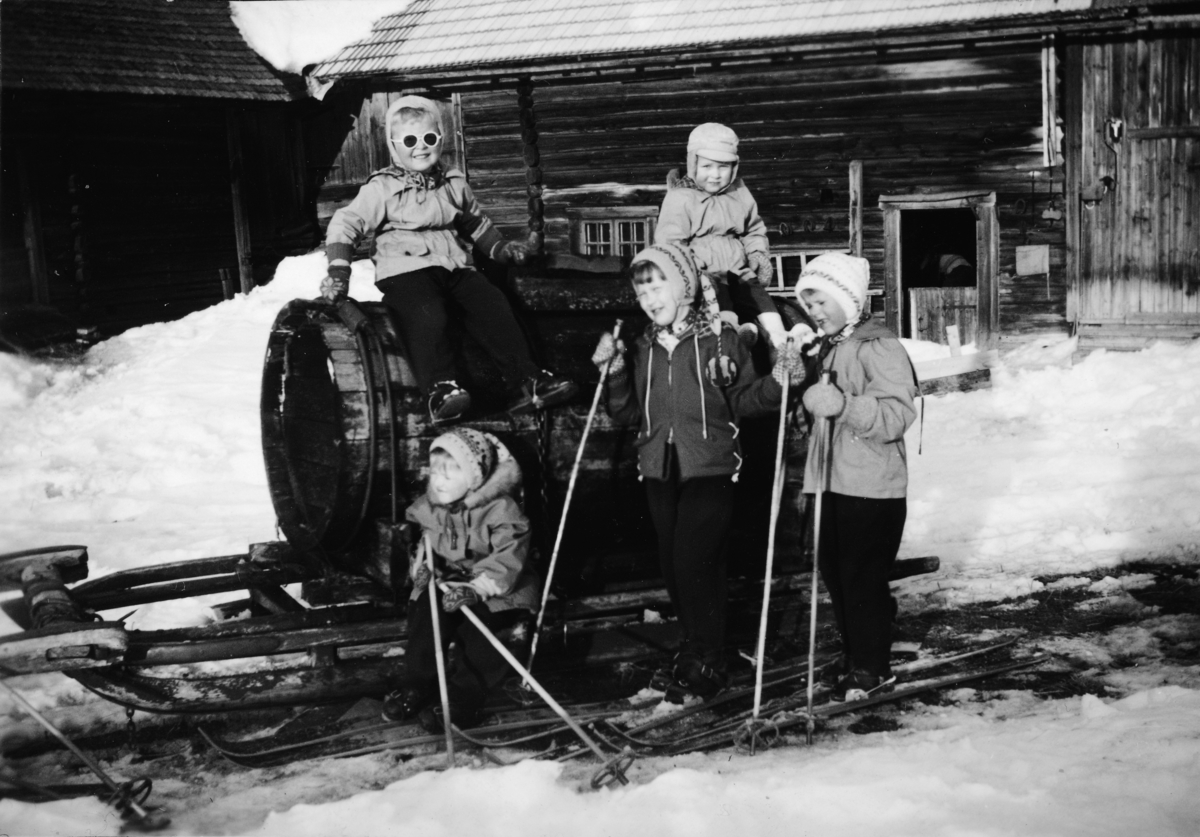 Ukjent, Jølstad i Vallset vinteren 1958. Barn på ski, ved vanntønne. T. v. på tønna Finn Ove Foss f. 1952, og Sigurd Karsen Fagerhaug f.. 1955. Foran t. v. Edel Helene Botten f. 1954, Eva Toril Foss f. 1949 og Brith Kari Fagerhaug. Tønna ble brukt til kjøring av vann på Jølstad.