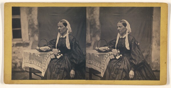Unknown, [Older woman seated at table, holding a small pair of binocular, basket on table top]