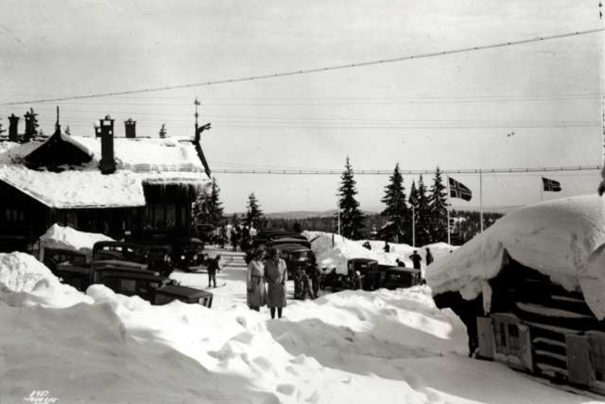 Hermann Christian Neupert, Frognerseteren Restaurant, Nordmarka, Oslo, Vintermotiv. Biler og mennesker foran restauranten. Flaggstenger med flagg.