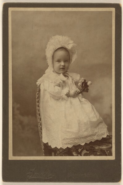 Smith, [Unidentified baby wearing a bonnet, holding a flower, seated]