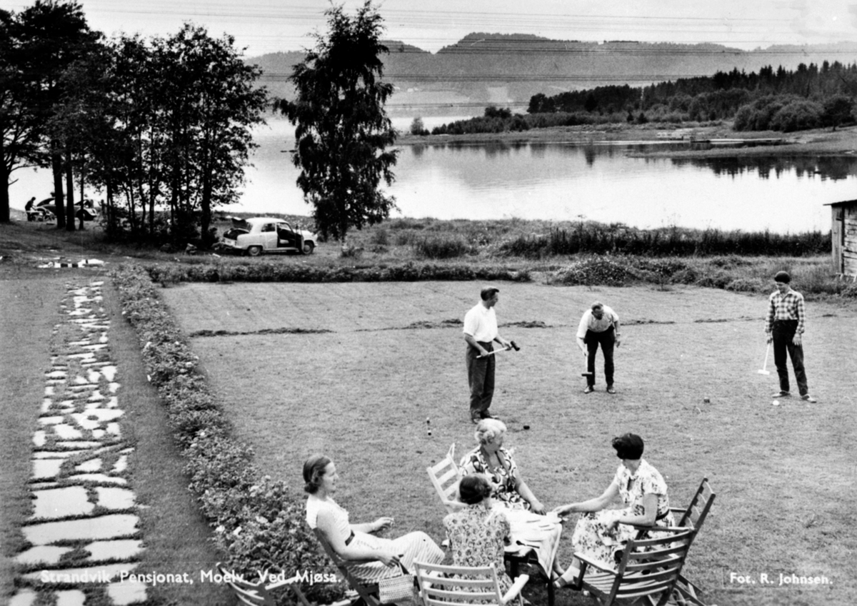 Anno Domkirkeodden, Strandvik pensjonat, Korgerstuvika, Moelv. Gruppe menn spiller krokket på plen. Gruppe damer drikker kaffe. Mjøsa i bakgrunn.