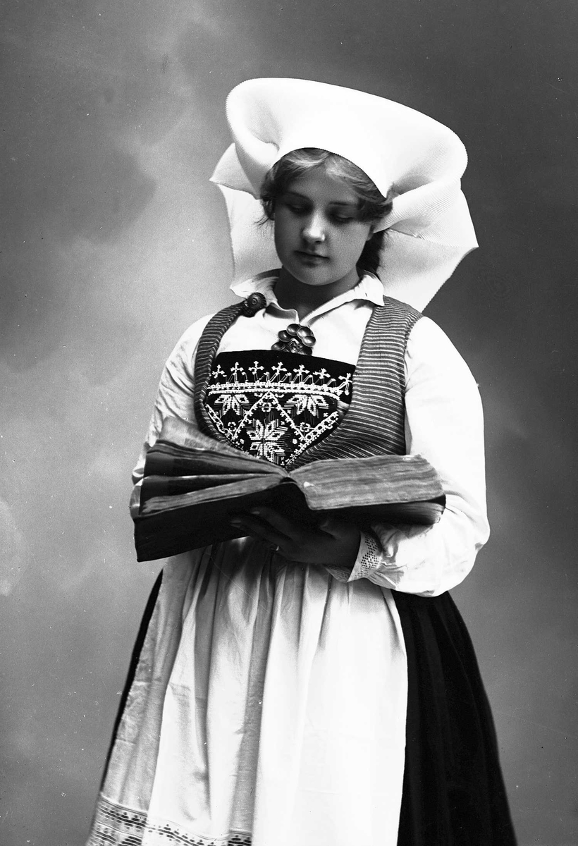 Solveig Lund, Studioportrett av kvinne i drakt og skaut. Hun holder en oppslått bok hendene. Bakgrunnen er nøytral.
