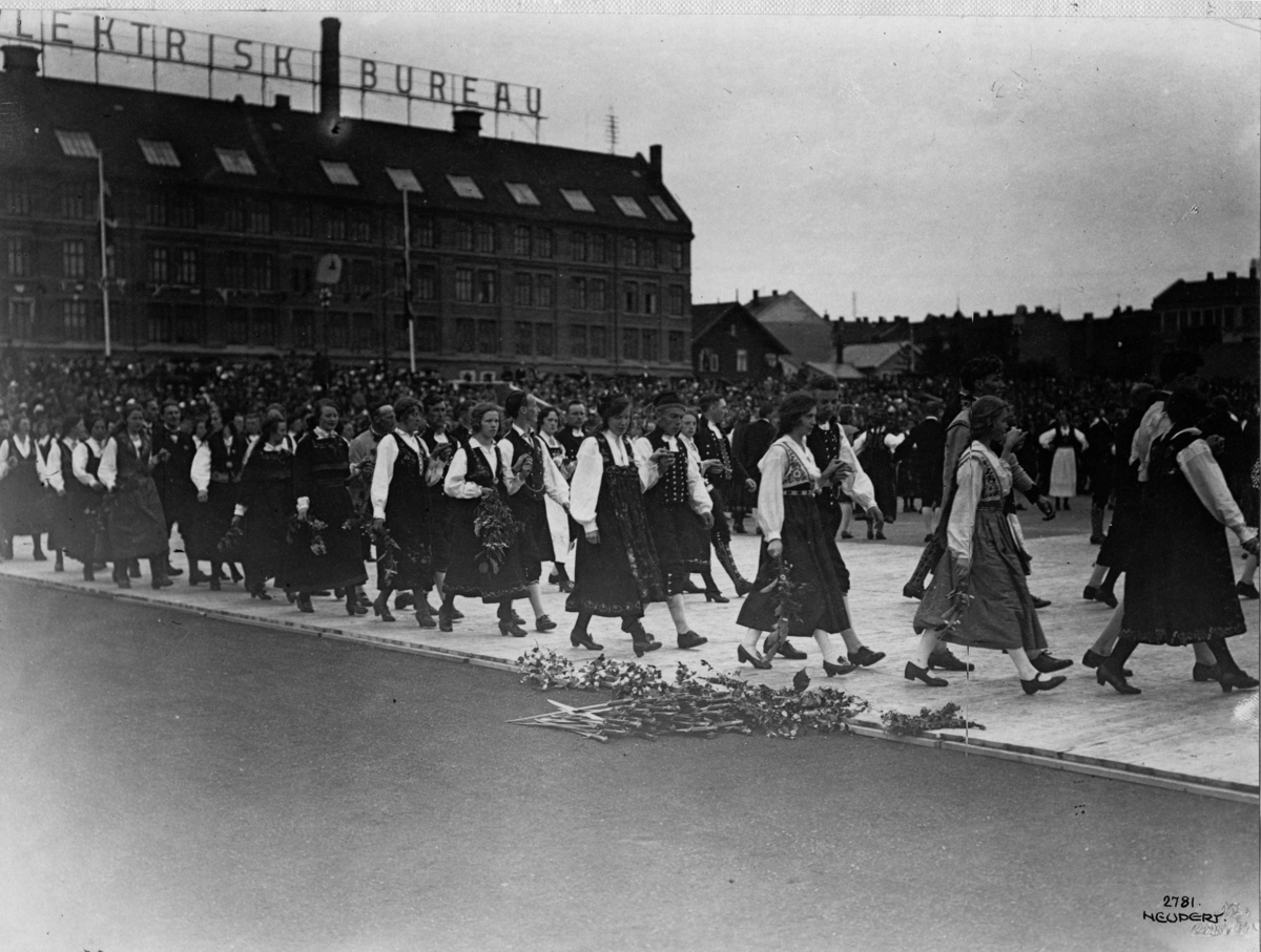 Hermann Christian Neupert, Folkedansstevne på Frogner Stadion 1925. Prosesjon. Bybebyggelse i bakgrunnen.