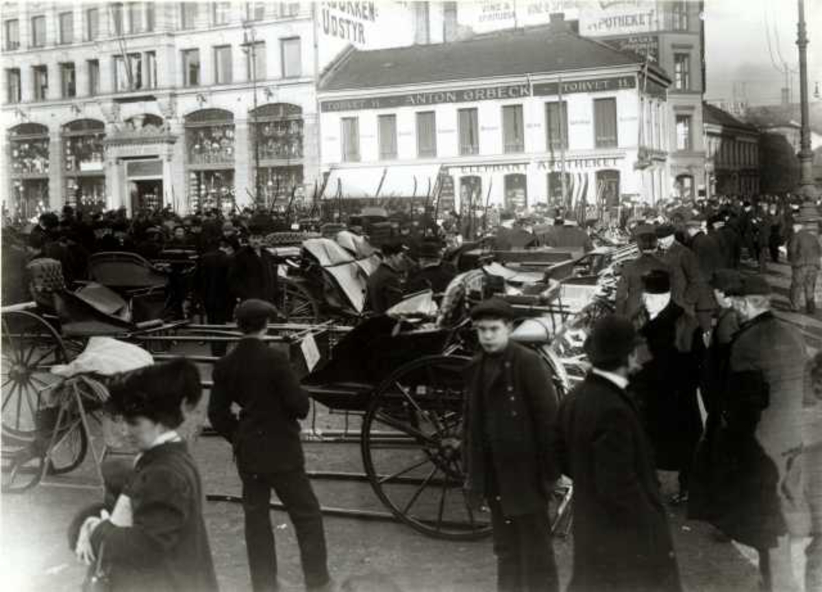 Hermann Christian Neupert, Stortorvet, Oslo 1911. Mennesker og hestevogner oppstilt utenfor Glasmagasinet..