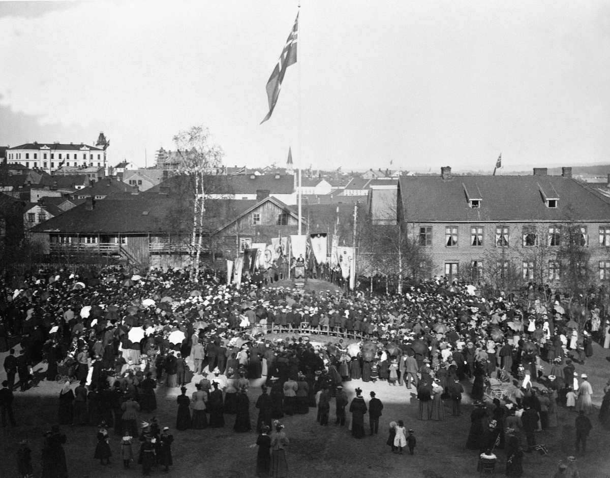 Anno Domkirkeodden, 17 mai feiring på skoletorget, Vestre Torg. Mye folk og flagg med unionsmerke. Korslundgården til venstre med smia. Røhr pensjonat til høyre. "Katta" leide lokaler i Røhr-gården.
