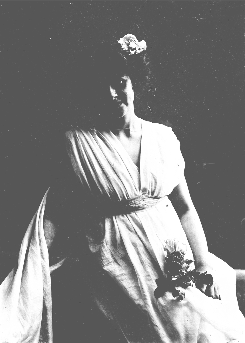 Solveig Lund, Studioportrett av kvinne i kostyme med hvit kjortel og blomster i håret. I den ene hånden holder hun en blomsterbukett.