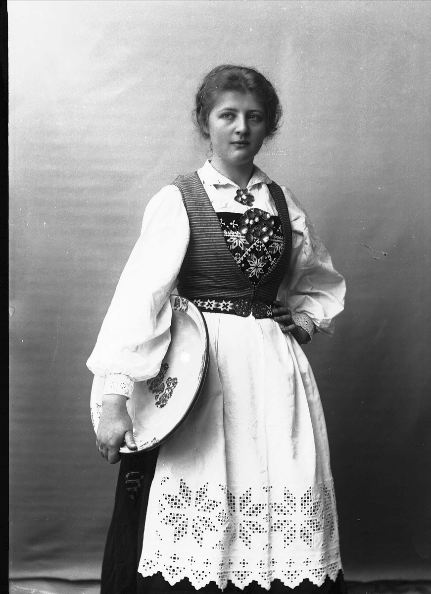 Solveig Lund, Studioportrett av kvinne i drakt, som holder et fat under høyre arm. Bakgrunnen er nøytral.