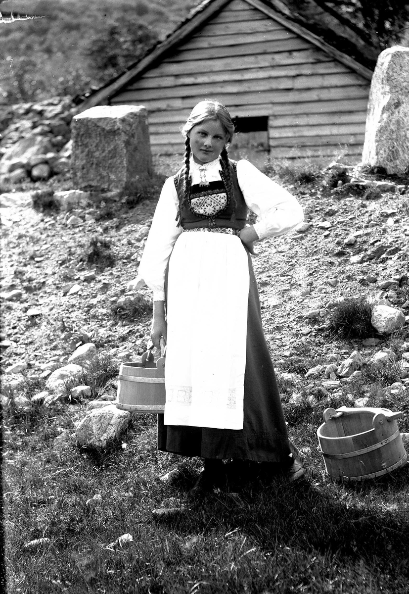 Solveig Lund, Jente i nasjonaldrakt stående på seter med to bøtter.