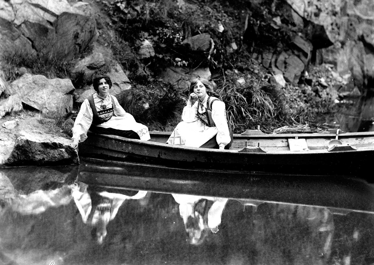 Solveig Lund, To kvinner i Hardangerdrakt sitter i robåt.