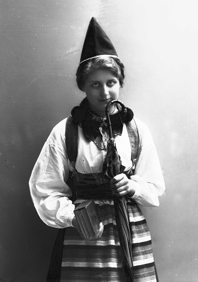 Solveig Lund, Kvinne i drakt og lue, som holder salmebok/bibel i en hånd og en paraply i den andre.