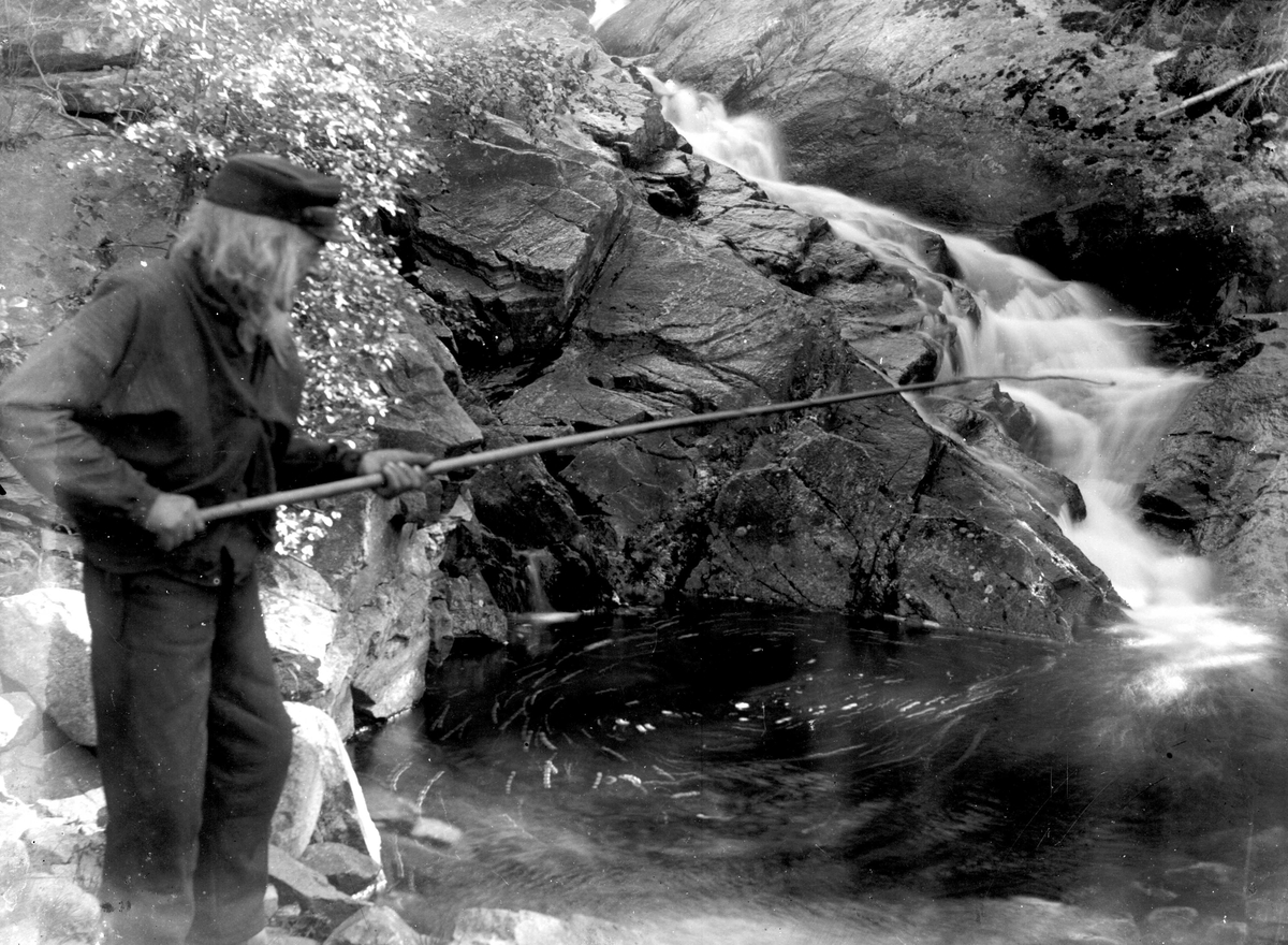 Juliane Fredrikke Langberg, Eldre mann i skyggelue fisker (?) med en lang stang nedenfor lite fossefall. Muligens i Eggedal. Fra malerinne Juliane Fredrikke Langbergs samling, tatt 1895-1910 med motivkrets slekt og venner samt steder tilknyttet samvær med disse.