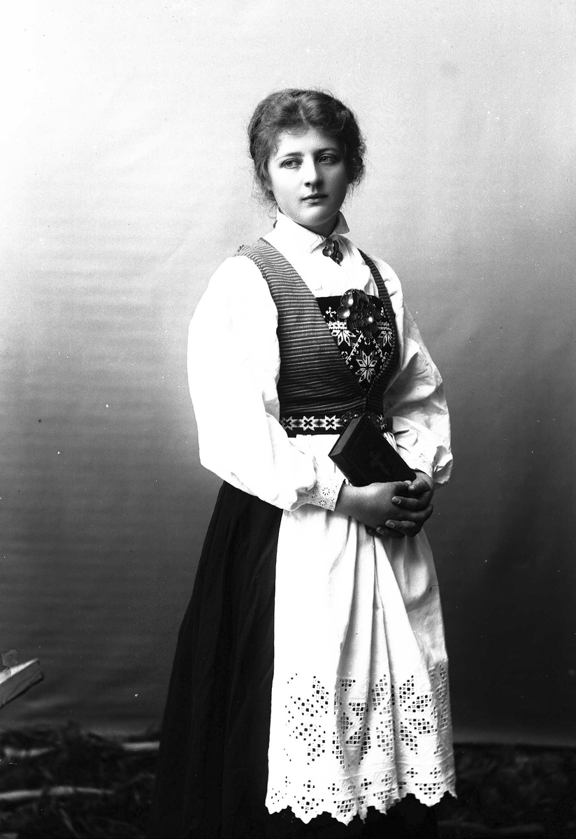 Solveig Lund, 3/4 dels studioportrett av kvinne i drakt, som holder en bok i hendene. Bakgrunnen er nøytral.