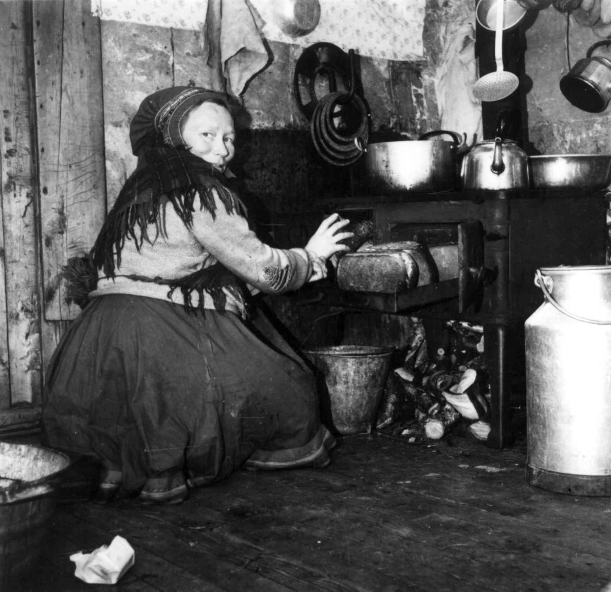 Virginia Raymond Davidson, Interiør fra et kjøkken. En kvinne, Kautokeinosame, steker brød i vedkomfyr. 1958.