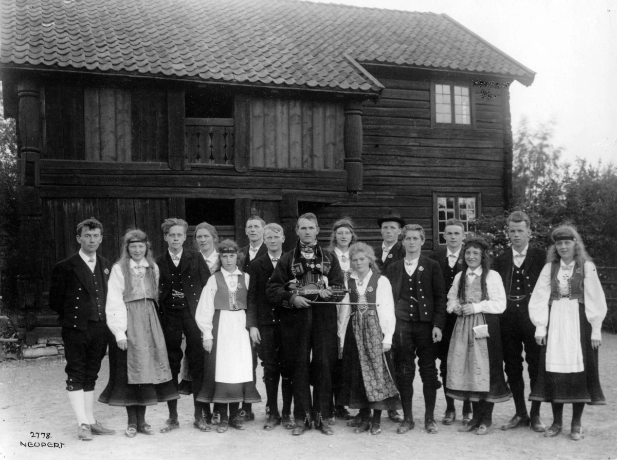 Hermann Christian Neupert, Folkedansstevne 1925. Dansere i folkedrakter. Felespiller i midten. I bakgrunnen tømmerhus.