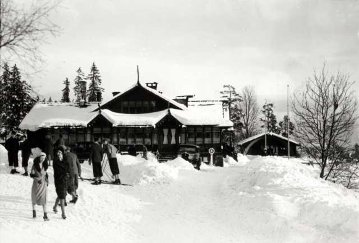 Hermann Christian Neupert, Frognerseteren Restaurant, Nordmarka, Oslo. Vintermotiv. Mennesker på ski og på bena foran restauranten.