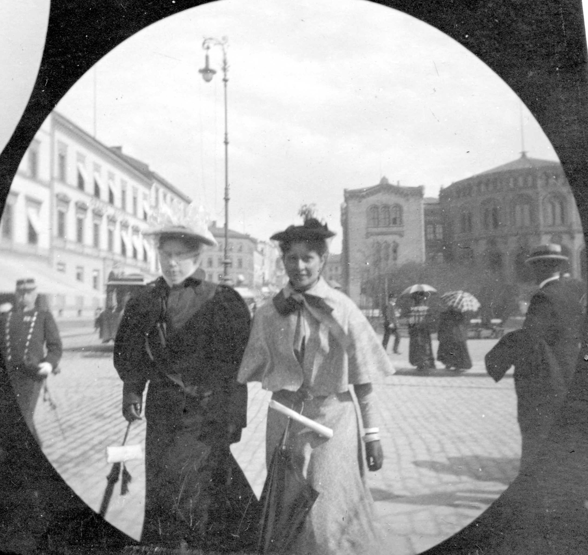 Fredrik Carl Mülertz Størmer, Frk. Ada Lund og frk. Ada Clauson, senere fru Størmer, spaserer langs Karl Johans gate, Oslo, med Stortinget i ryggen og Grand Hotell på den andre siden av gata.